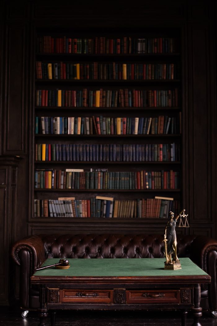 services-05 A sophisticated library scene featuring a leather sofa, bookshelves, and a statue of justice with a gavel on the table.