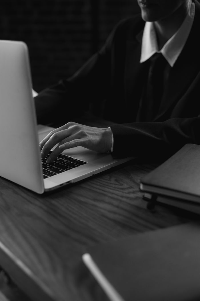 services-09 A business professional wearing a suit types on a laptop, captured in a grayscale artistic style.