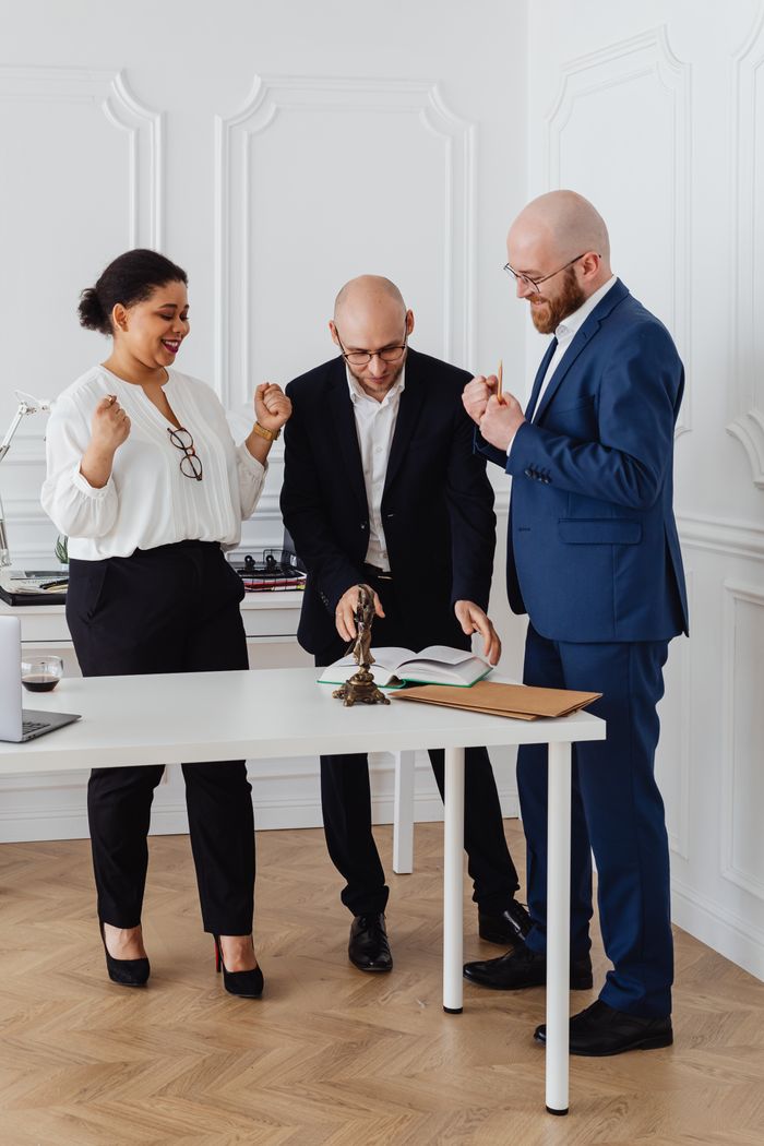 Three business professionals celebrate a successful deal in a modern office setting.